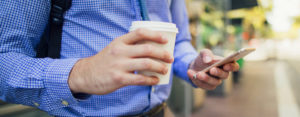 man holding cell phone and coffee